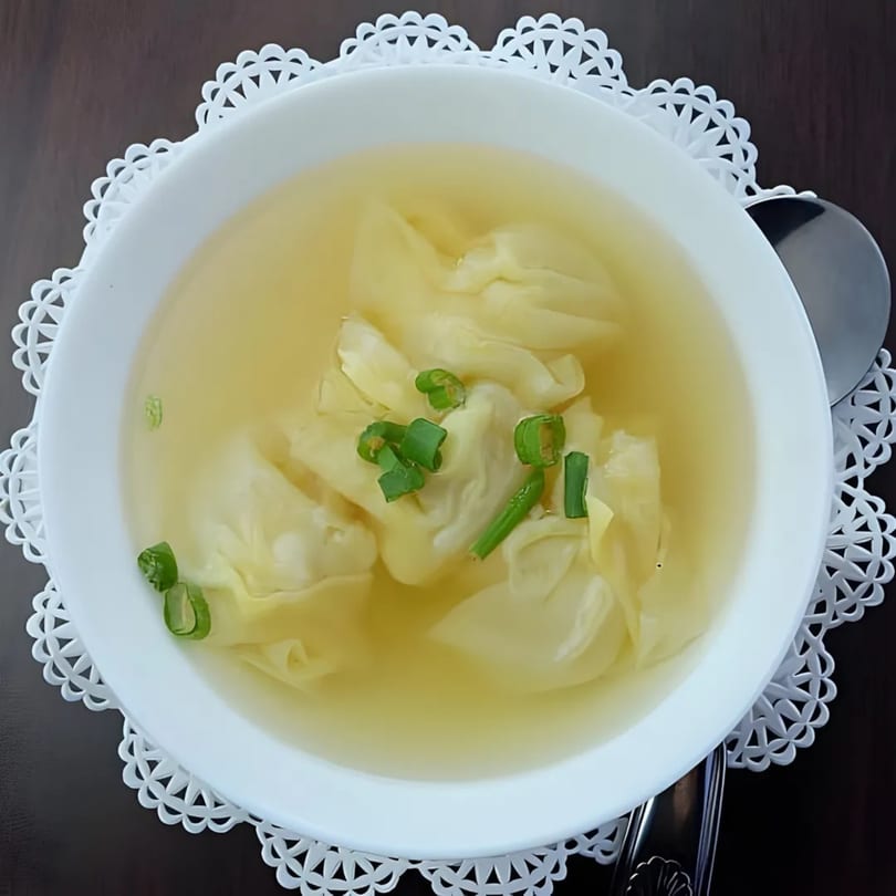 Wonton soup with green onions in a white bowl on a white lace placemat at Spice Thai Kitchen.