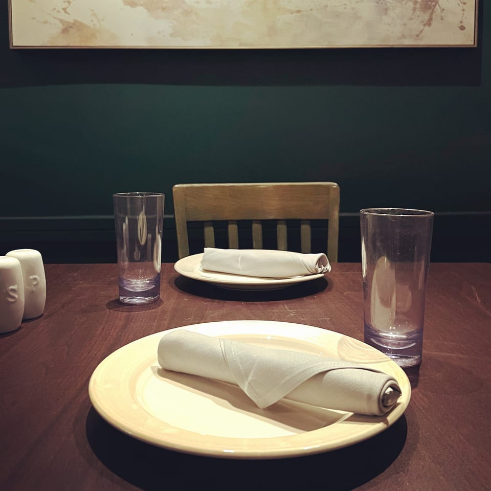 Table set for two at Spice Thai Kitchen, with plates, rolled napkins, and glasses.