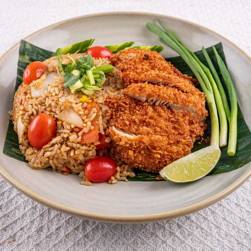 Thai fried rice with crispy chicken, cherry tomatoes, green onions, and a lime wedge.