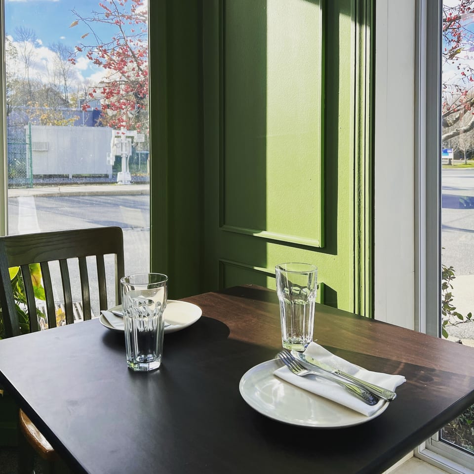 A set table with plates, cutlery, and glasses next to a window with green walls.