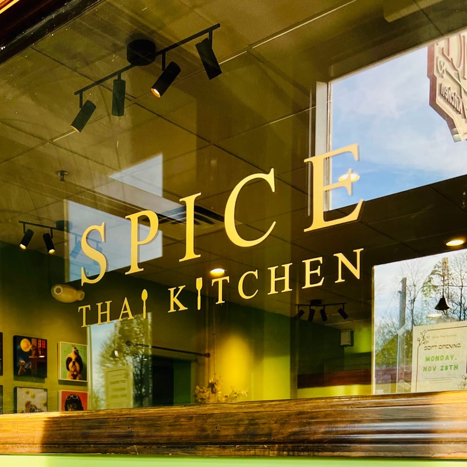The Spice Thai Kitchen sign on a glass window, reflecting the sky and trees.