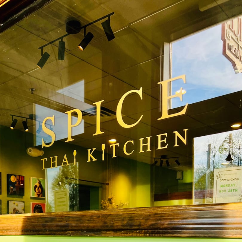 The Spice Thai Kitchen sign on a glass window, reflecting the sky and trees.
