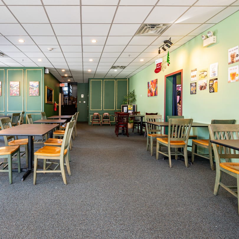 Interior of Spice Thai Kitchen with green walls, gray carpet, and empty tables with wooden chairs.