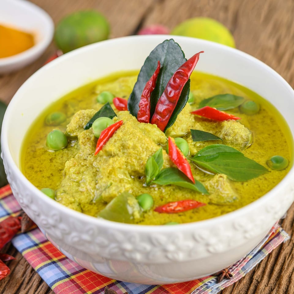 Spice Thai Kitchen's green curry in a white bowl, garnished with red chilies and basil.