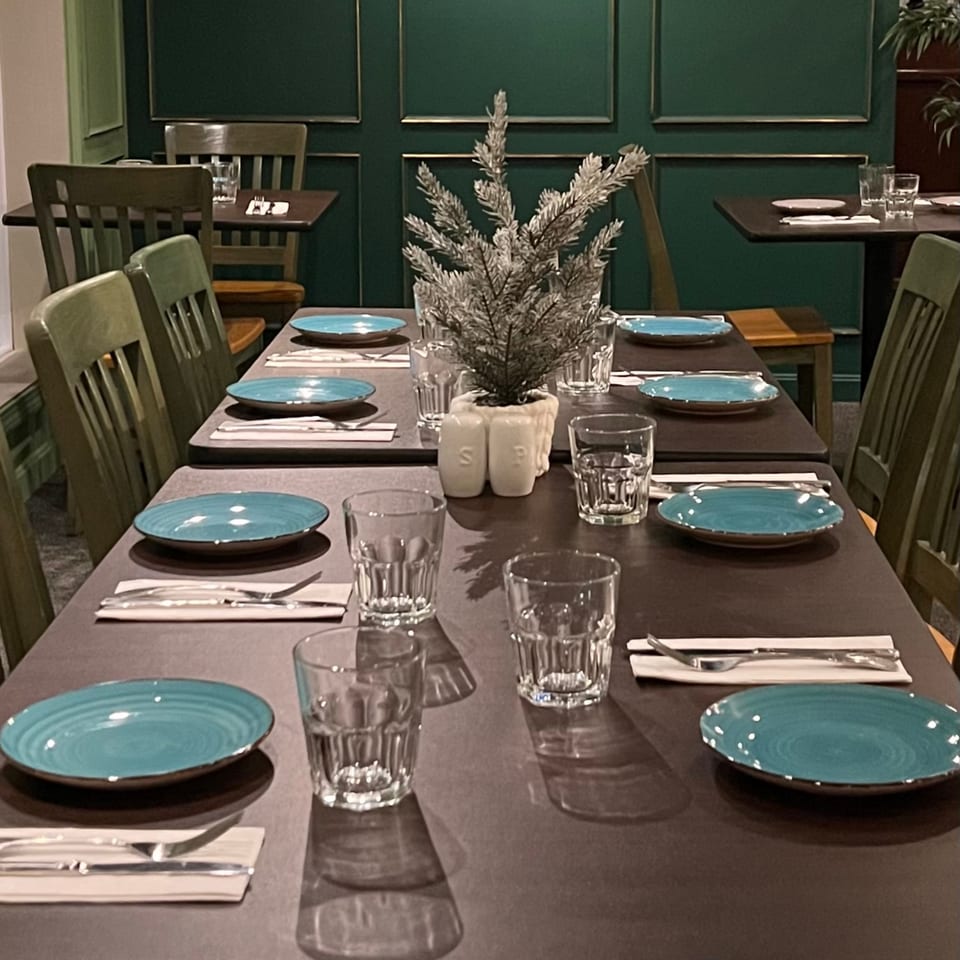 Set tables with teal plates, glasses, and cutlery in a dark green dining room at Spice Thai Kitchen.