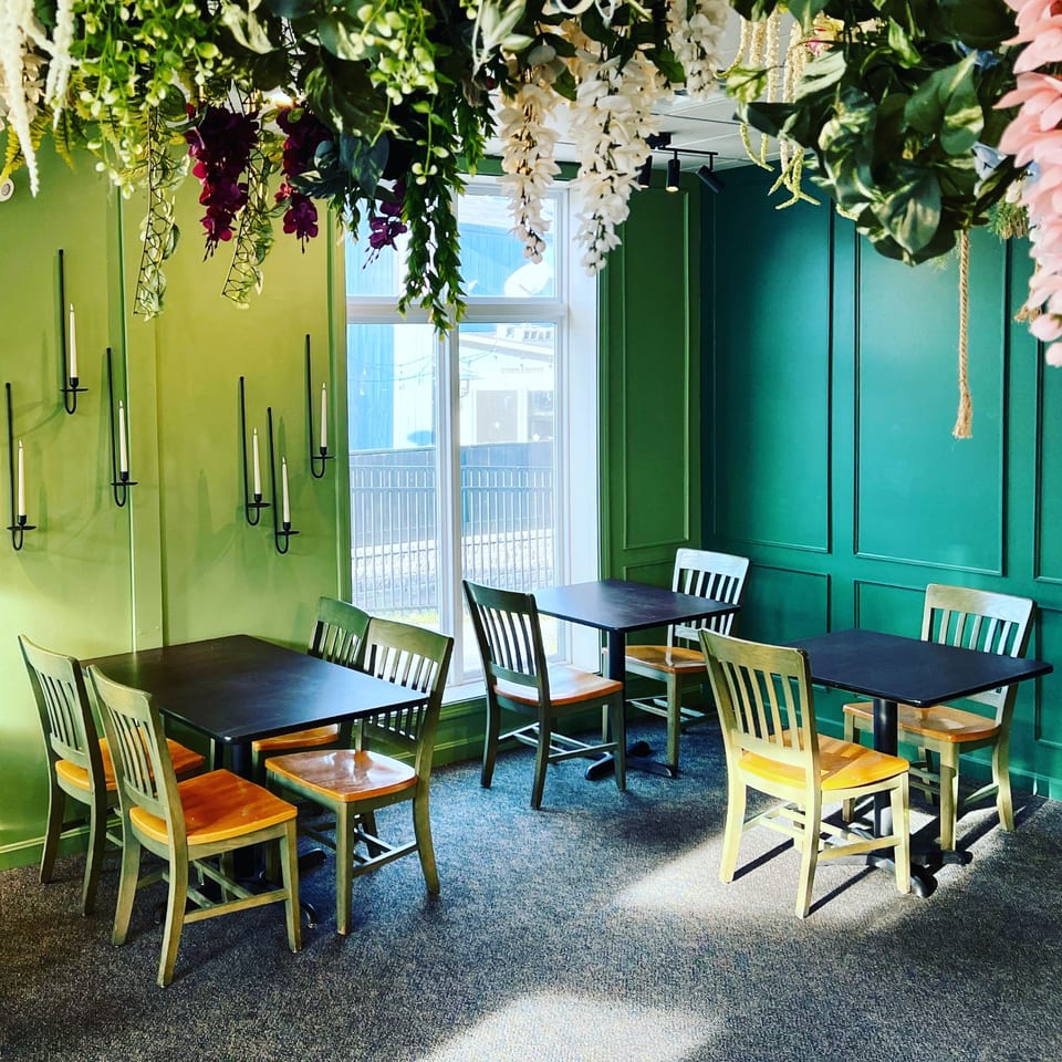 Spice Thai Kitchen dining area with green walls, black tables, and hanging floral decorations.